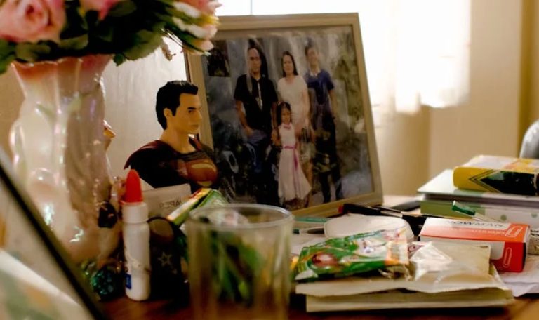 A table with a family photo, Superman figurine, books, and stationery, reflecting a personal and lived-in space.