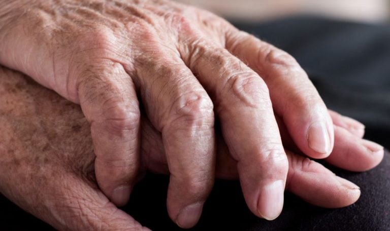Close-up of elderly hands gently resting together, symbolizing companionship, care, and emotional support in a peaceful setting.