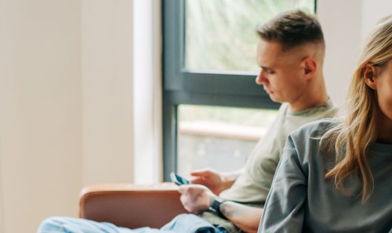 A couple sitting apart on a couch, both looking distant and thoughtful, suggesting tension or emotional disconnection in their relationship.
