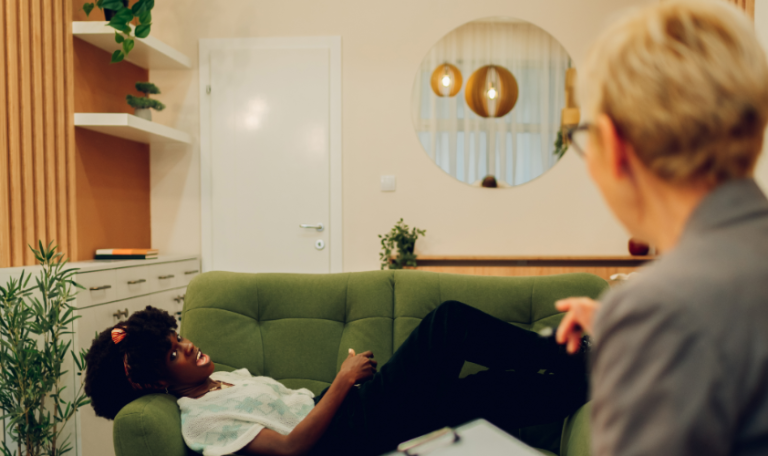 The camera focuses on the woman lying down on a sofa at the background as she talks to her therapist.