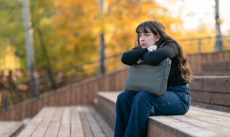 Teen girl sitting alone in autumn park looking thoughtful, symbolizing seasonal mental health changes and emotional reflection in fall.